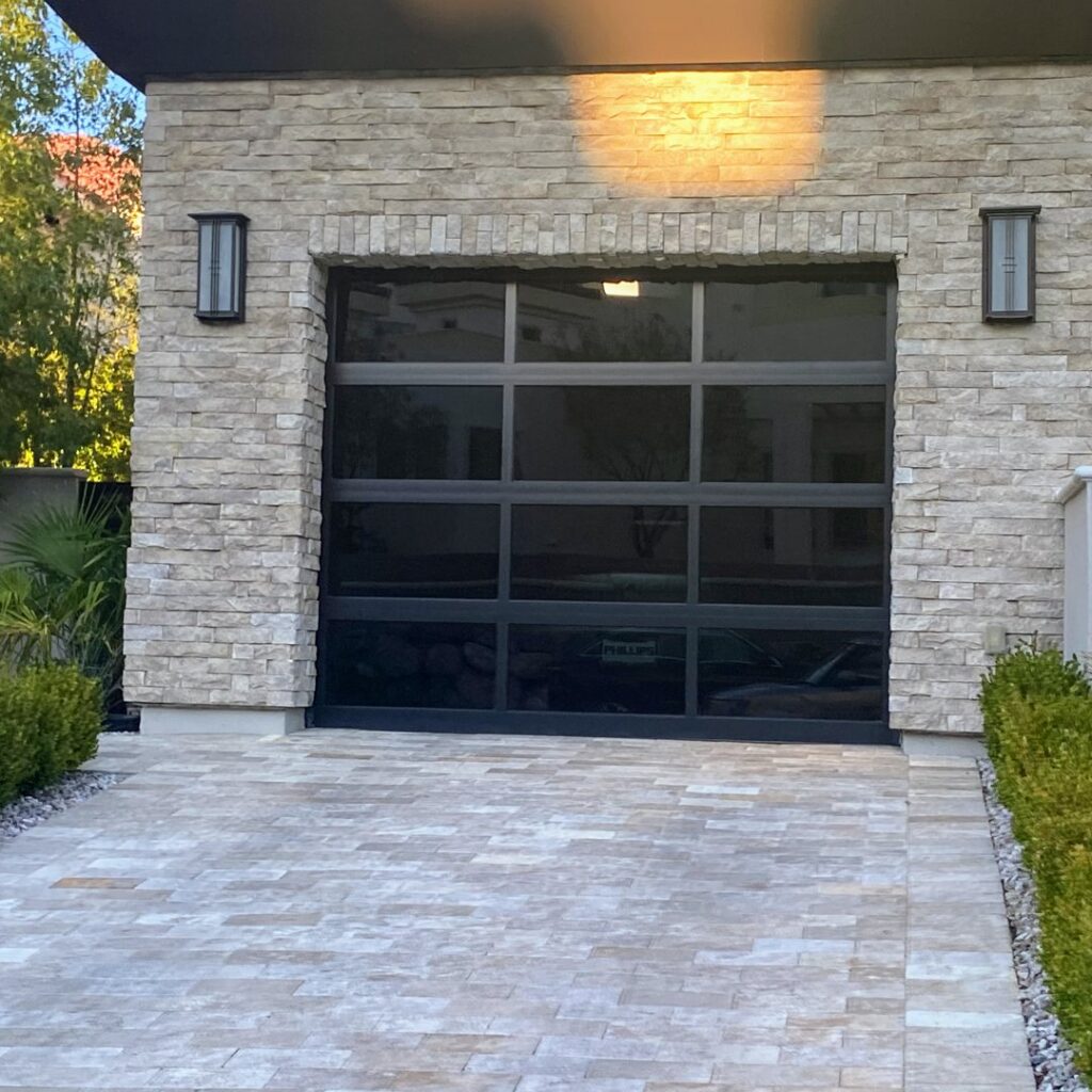 A sleek black glass garage door installed on a modern stone-faced home, showcasing a premium service by American Veteran Garage Door Repair Henderson, NV.
