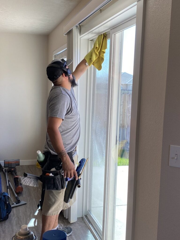 A professional cleaning a sliding glass door with a squeegee and cloth by Idaho Gem Cleaning in Caldwell, ID.