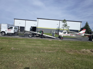 Montes Towing Services truck assisting with the transport of a small airplane on a specialized trailer in Indianapolis, IN.