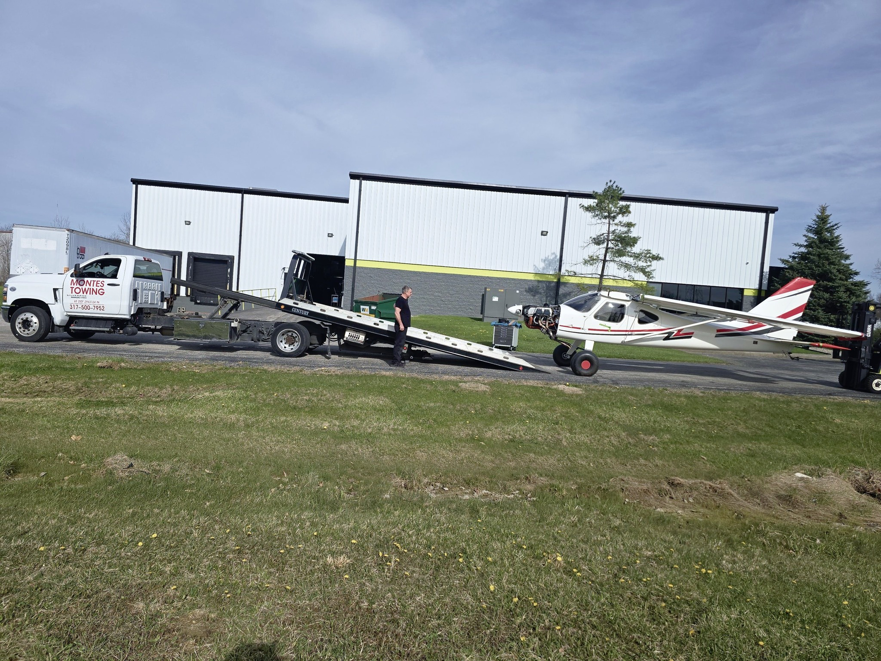 Montes Towing Services truck assisting with the transport of a small airplane on a specialized trailer in Indianapolis, IN.