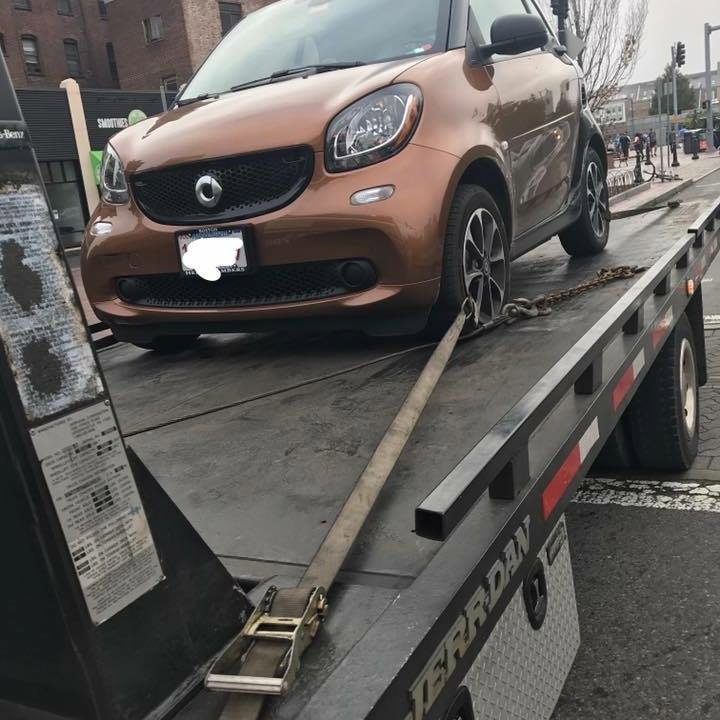 A small brown car secured on a flatbed tow truck by Milan Towing inc. in Milan, MI.