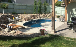 A small kidney-shaped swimming pool with a waterfall feature and surrounding patio by Backyard Escapes by Kerner Pools & Spas in Bismarck, ND.