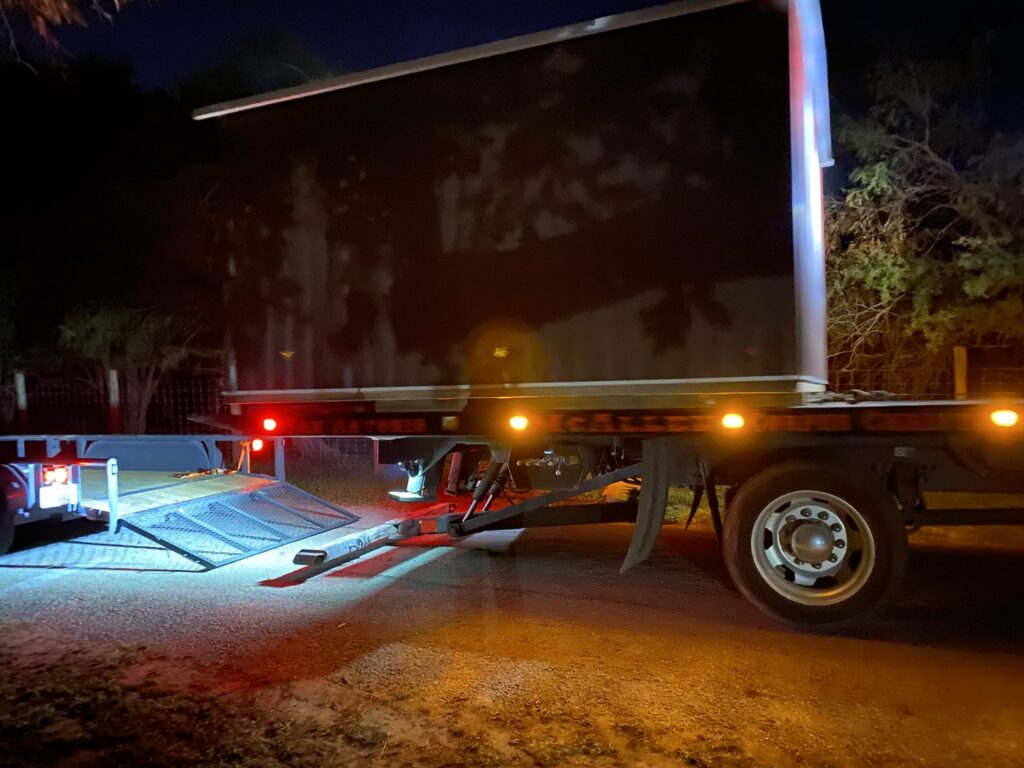 A CC Wrecker Service flatbed tow truck preparing to haul a small black trailer at night in Corpus Christi, TX.