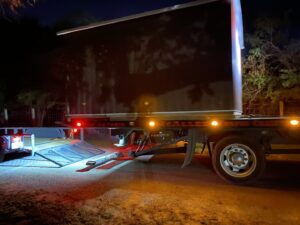 A CC Wrecker Service flatbed tow truck preparing to haul a small black trailer at night in Corpus Christi, TX.