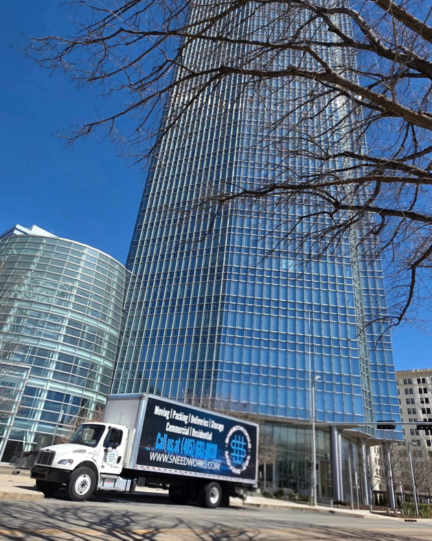 A SNEEDWORKS moving truck parked in front of a commercial building in Oklahoma City, OK, ready for a job.