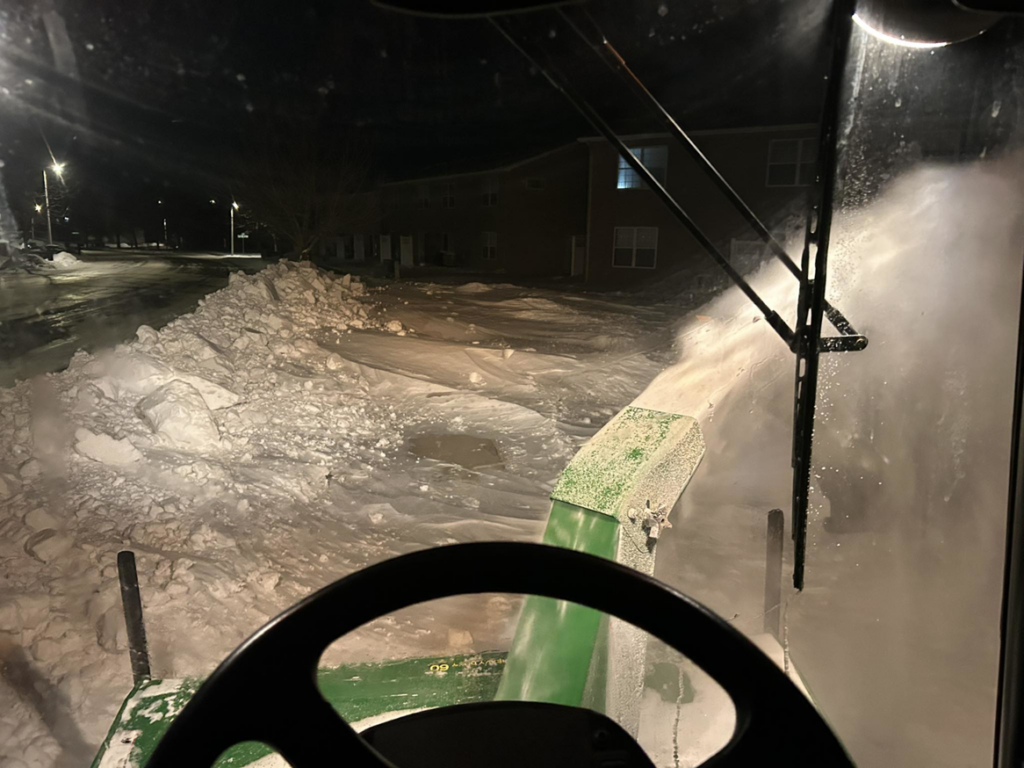 A snow blower attachment on a tractor clearing a driveway at night for Rochester Ground Lawn & Snow Services in Rochester, MN.