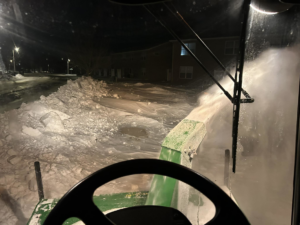 A snow blower attachment on a tractor clearing a driveway at night for Rochester Ground Lawn & Snow Services in Rochester, MN.