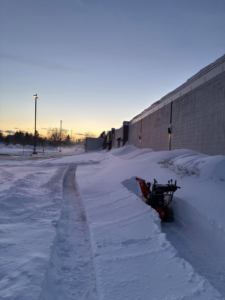 A snow blower actively clearing a deep snow path next to a commercial building by Pro Cut Lawn Services in Green Bay, WI.
