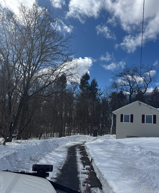 A residential driveway partially cleared of snow by Diamond Image in New Haven, CT, with snow piled on the sides.