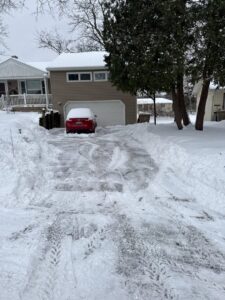 A residential driveway with snow cleared to the sides by Snow Scholars - Snow Removal By College Students in Madison, WI.