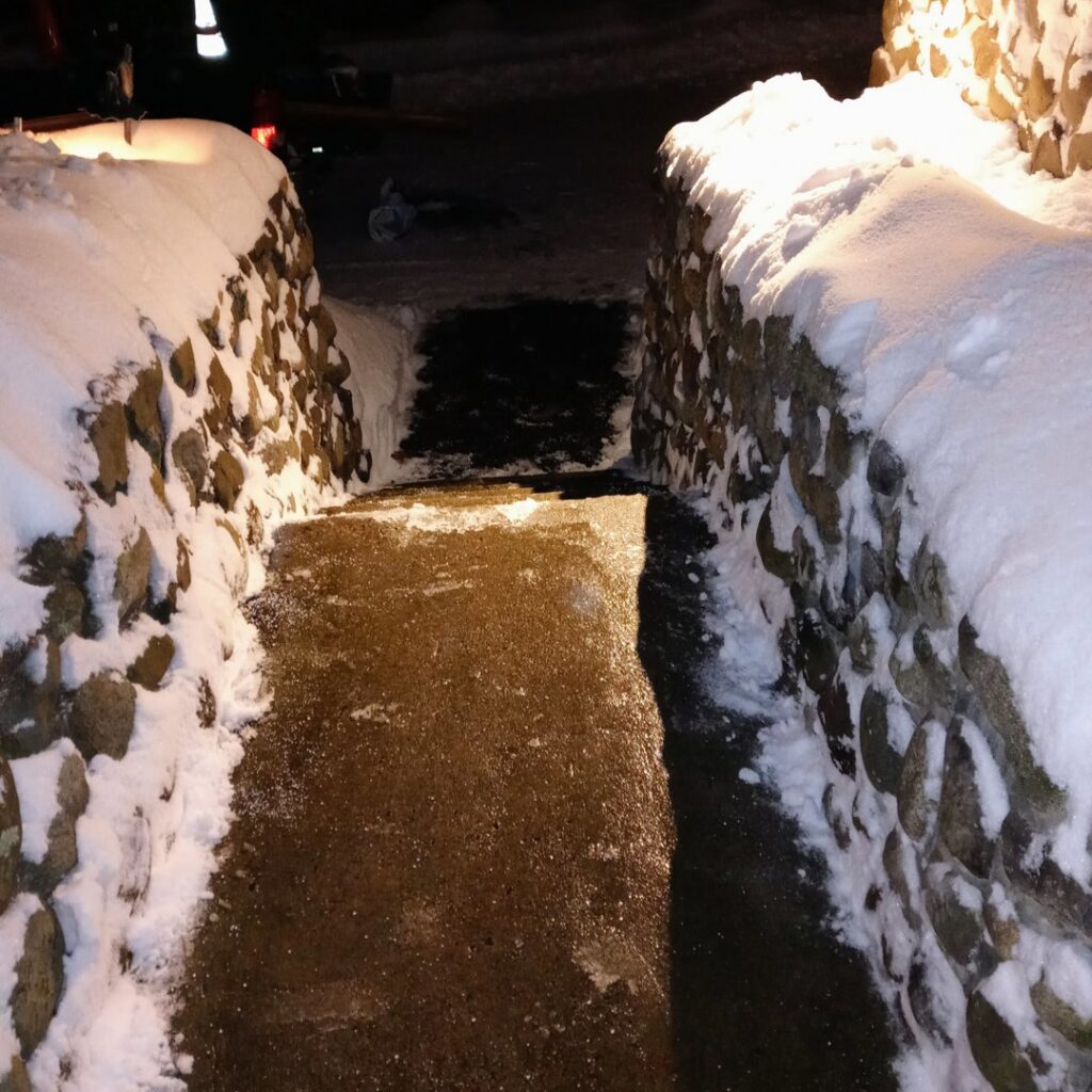 A pathway between stone walls completely cleared of deep snow, showcasing services by JG Lawn Care and Snow Removal, LLC in Albany, GA.