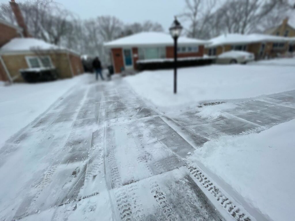 A residential driveway being cleared of snow with tire tracks visible by Evo Lawn & Landscape LLC in Waukegan, IL.
