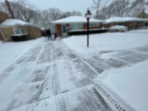 A residential driveway being cleared of snow with tire tracks visible by Evo Lawn & Landscape LLC in Waukegan, IL.