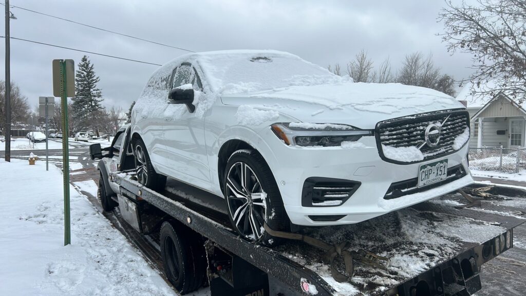 A snow-covered white SUV being transported on a flatbed tow truck by A-ROD Towing in Denver, CO.
