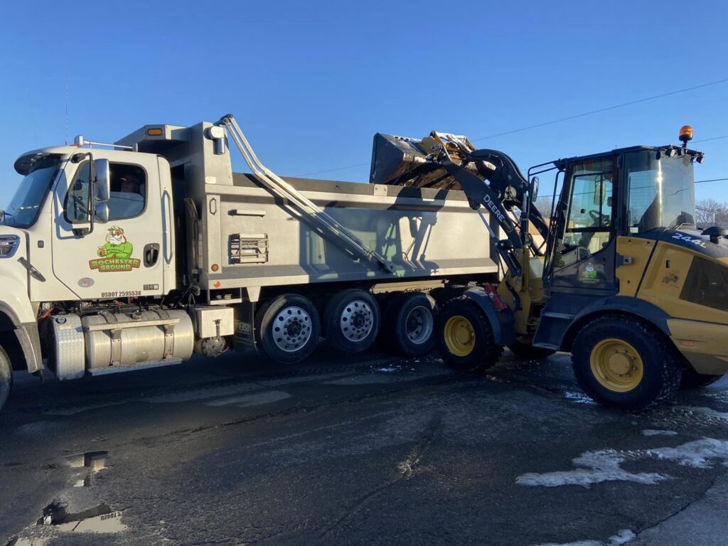 A dump truck being loaded with snow by a front-end loader for Rochester Ground Lawn & Snow Services in Rochester, MN.