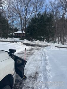 A white pickup truck with a snow plow clearing a residential driveway, with snow piled high, by Diamond Image in New Haven, CT.