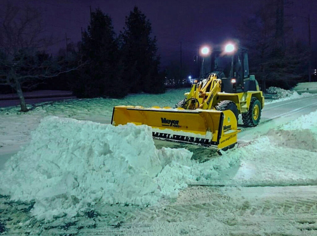 A yellow snow plow clearing a parking lot at night for ASAP Mow & Snow, LLC in Toledo, OH
