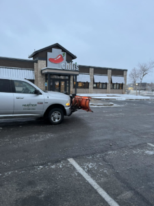 A Hunter Lawn Services snow plow truck parked in a Chili's restaurant parking lot after snow removal in Edmond, OK.
