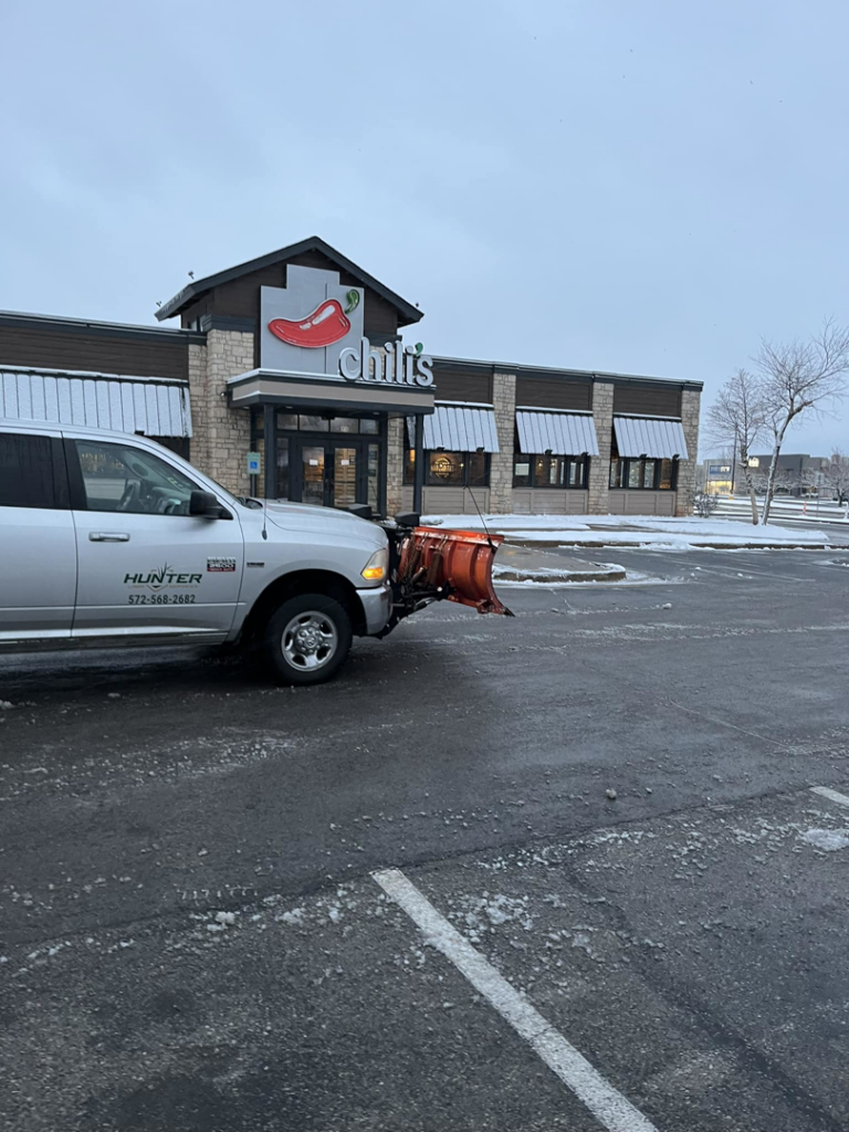 A Hunter Lawn Services snow plow truck parked in a Chili's restaurant parking lot after snow removal in Edmond, OK.