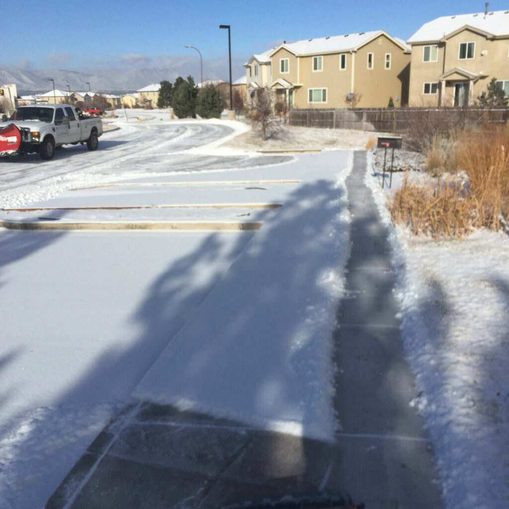 A snow plow truck from TLC Lawn Care and Snow Removal LLC clearing a parking lot in Colorado Springs, CO.