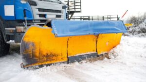 A large snow plow truck with a yellow blade actively clearing snow from a road for JC Snow Management in Mount Vernon, NY