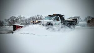 A JD Lawn Care LLC snow plow truck actively clearing a snowy road in Berea, OH.