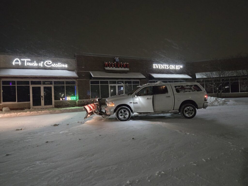 Snow plow truck in commercial parking lot at night, ready for snow removal by Brinkley'lawn service in Brooklyn Park, MN.