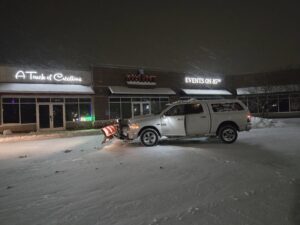 Snow plow truck in commercial parking lot at night, ready for snow removal by Brinkley'lawn service in Brooklyn Park, MN.