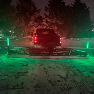 A snow plow truck with green lights clearing snow at night by David's Lawn Service in Plymouth, MN