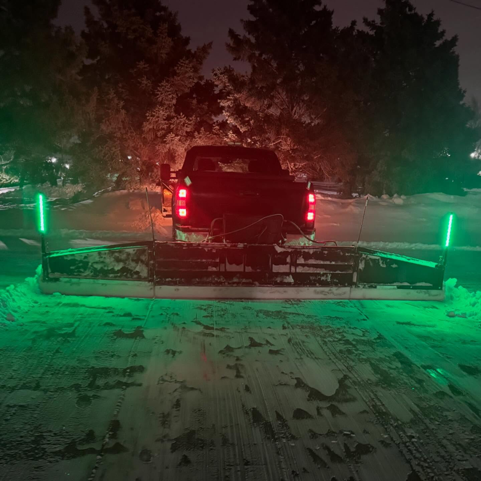 A snow plow truck with green lights clearing snow at night by David's Lawn Service in Plymouth, MN