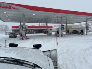 A snow plow truck clearing snow from a gas station parking lot by Lovett lawn care & snow removal in Omaha, NE.