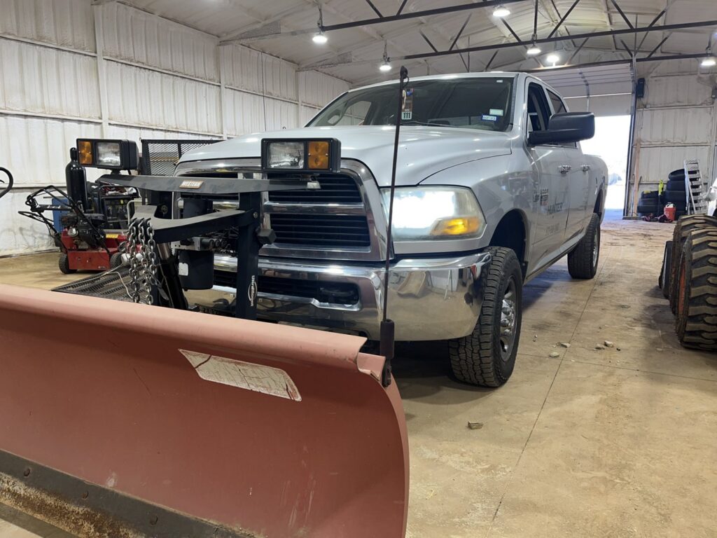 A Hunter Lawn Services snow plow truck with a plow attachment parked inside a garage in Edmond, OK.