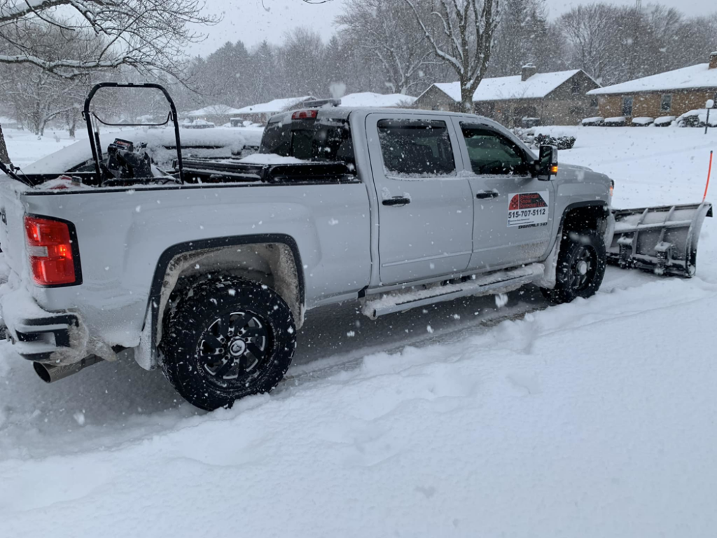 A silver snow plow truck from American Snow Removal LLC clearing snow on a residential street in Des Moines, IA.