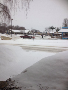 A red pickup truck with a snow plow on a snowy street, ready for snow removal by Haynes Snow Removal & Lawn Maintenance in Madison, WI.