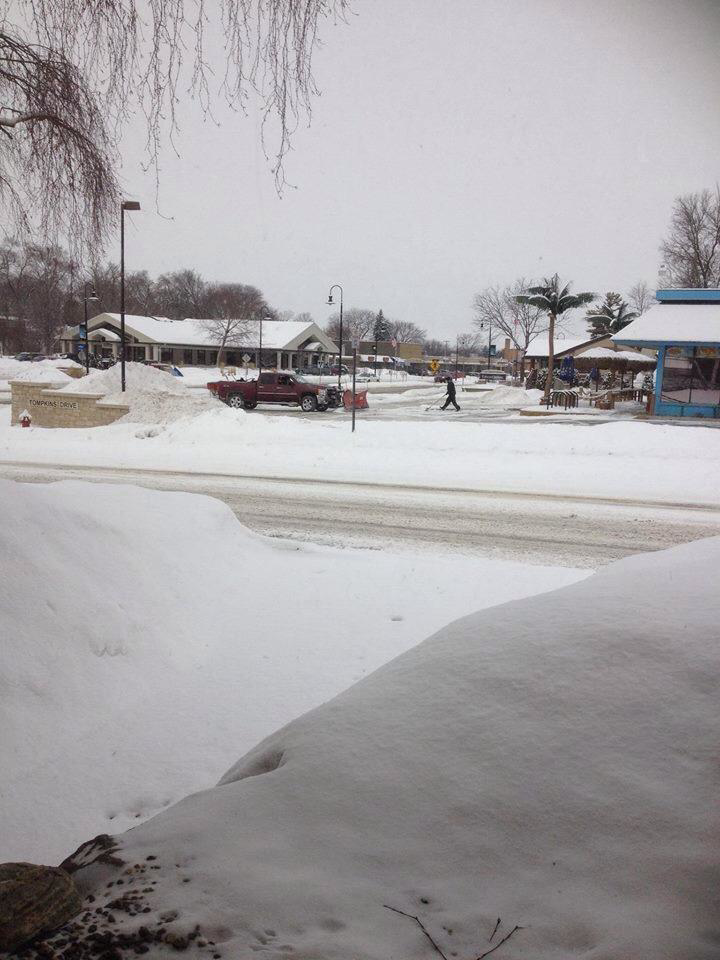 A red pickup truck with a snow plow on a snowy street, ready for snow removal by Haynes Snow Removal & Lawn Maintenance in Madison, WI.