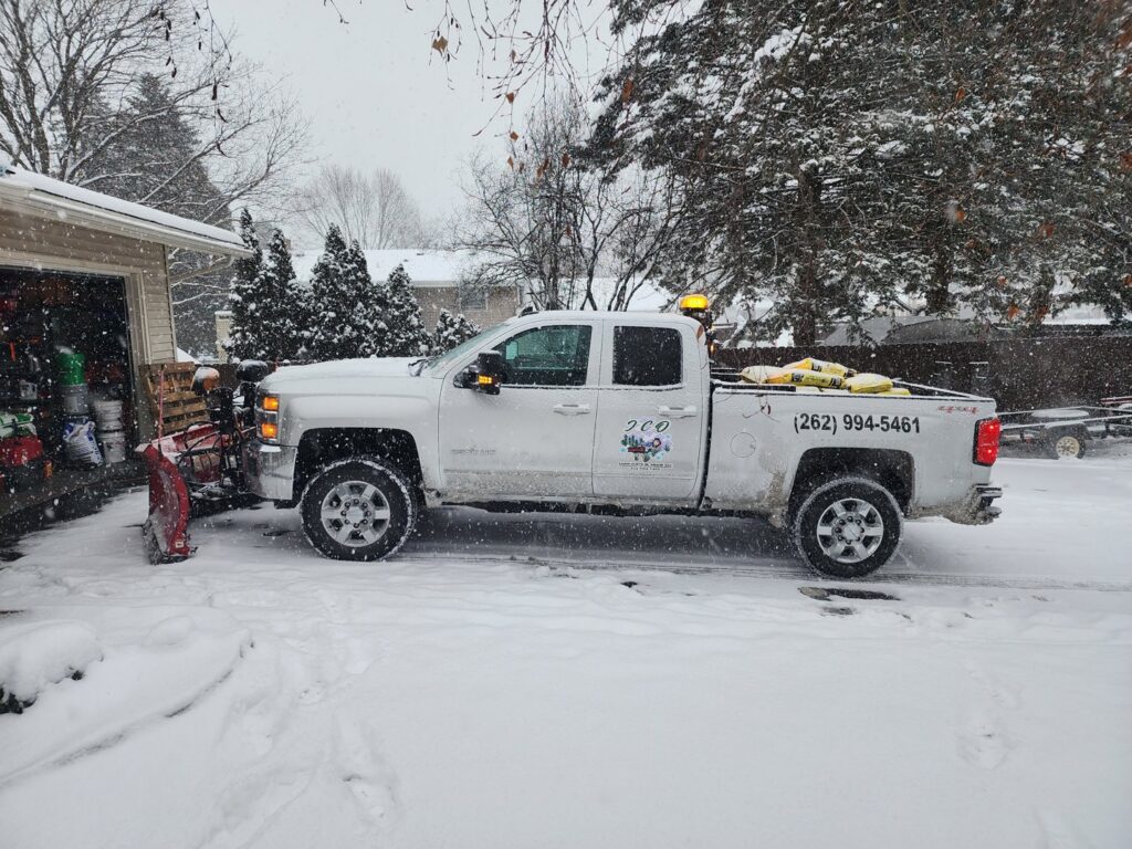A white pickup truck equipped with a snow plow and salt spreader, ready for snow removal services by JCO Landscape & SNOW in Racine, WI.
