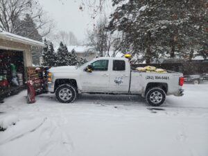 A white pickup truck equipped with a snow plow and salt spreader, ready for snow removal services by JCO Landscape & SNOW in Racine, WI.
