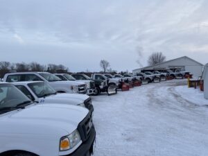 A line of pickup trucks equipped with snow plows, parked in a snowy lot, ready for snow removal by C&S Lawncare in Ann Arbor, MI.