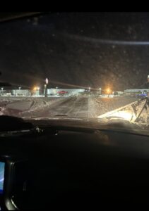 A snow plow clearing a commercial parking lot at night, provided by First Class Lawn Care and Snow Removal LLC in Shawnee, KS.