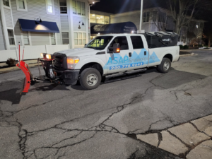 A white snow plowing truck with a front plow and rear salt spreader, ready for service by American Snow Plowing Services in Rockville, MD.