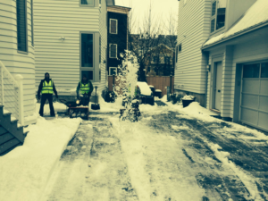 A snow removal crew from Snow Way Boston clearing a residential driveway with a snow blower and shovel in Cambridge, MA.