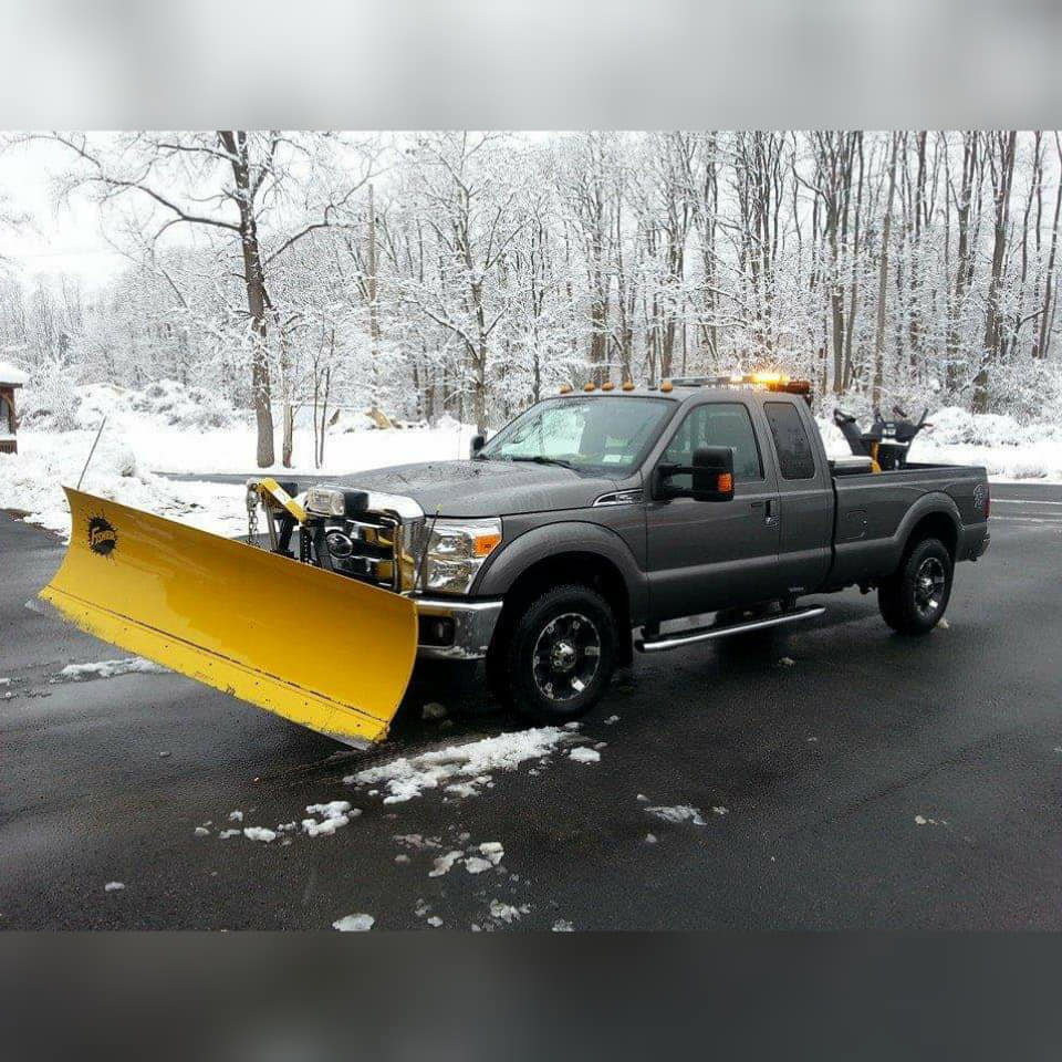A fleet of snow removal trucks with plows and salt spreaders, and a tractor, ready for night operations by TPM Snow Removal in Schenectady, NY.