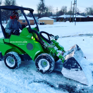 A Grounded Lawn Landscaping crew member operates a small loader with a snow bucket for snow removal in Thornton, CO.