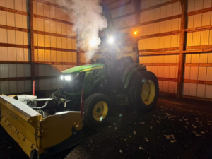 A green tractor equipped with a snowplow inside a garage, ready for snow removal by Pro Cut Lawn Services in Green Bay, WI.