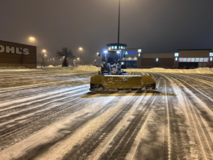 A John Deere snowplow clearing a large commercial parking lot at night for Cities Lawn and Snow LLC in Woodbury, MN.