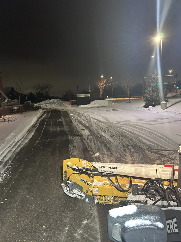 A snowplow clearing a road or driveway at night, showing effective snow removal by Cities Lawn and Snow LLC in Woodbury, MN.