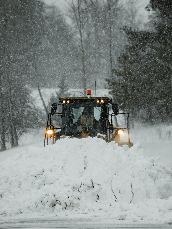 A large yellow snowplow clearing a road during a snowfall for Elcor Construction in Rochester, MN.