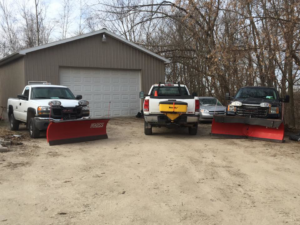 Three snowplow trucks, one with a salt spreader, ready for snow removal by Total Lawn Care & Snowplowing in Littleton, CO.