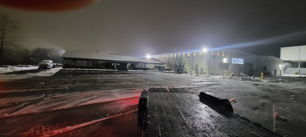 A large snowy parking lot at night with cleared snow piles, showcasing Yard Monkeys' snow removal in Hixson, TN.
