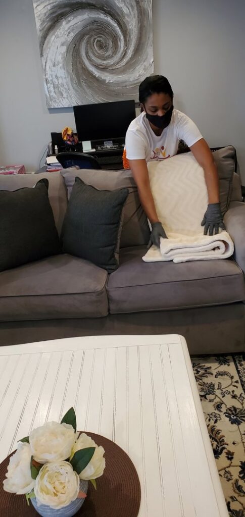 A house cleaner tidying a blanket on a sofa in a living room for TAG Team Cleaning of West Hartford, CT